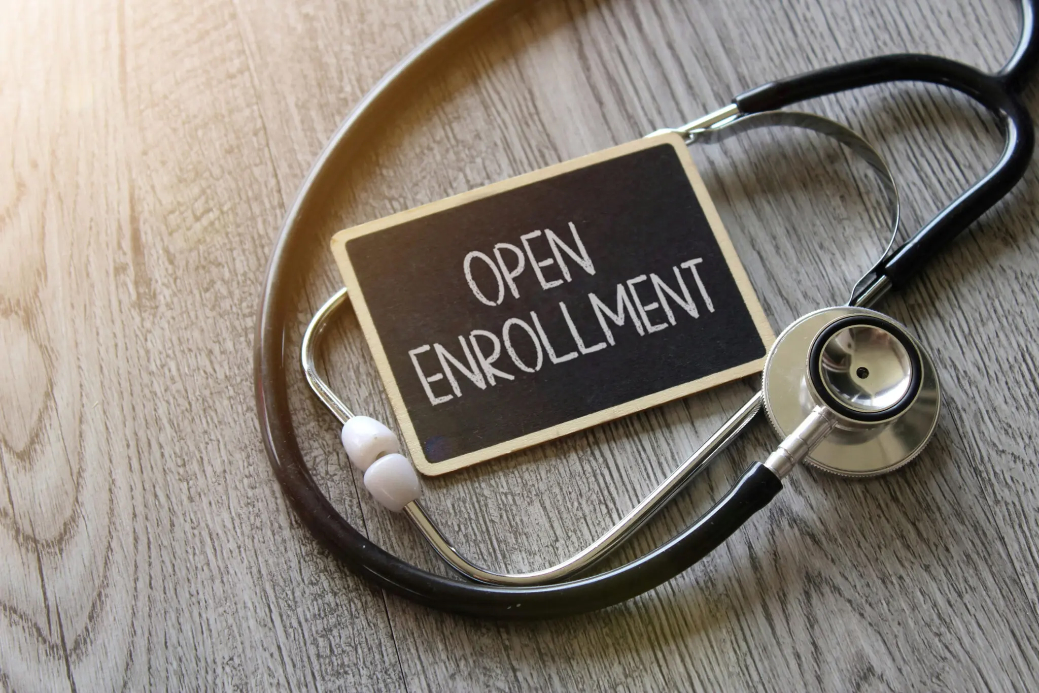 Stethoscope and chalkboard with text OPEN ENROLLMENT on wooden table.