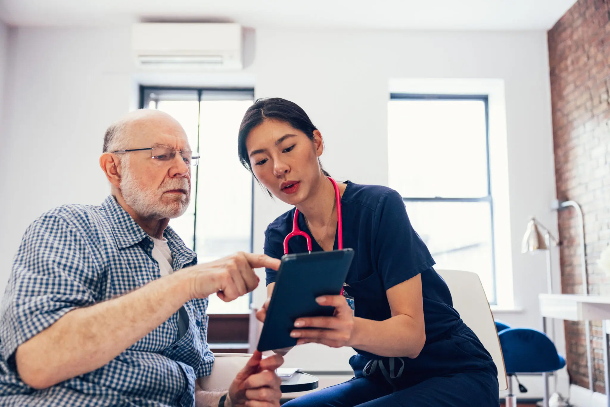 "Nurse and her patient checking medical information on a tablet during a routine appointment"