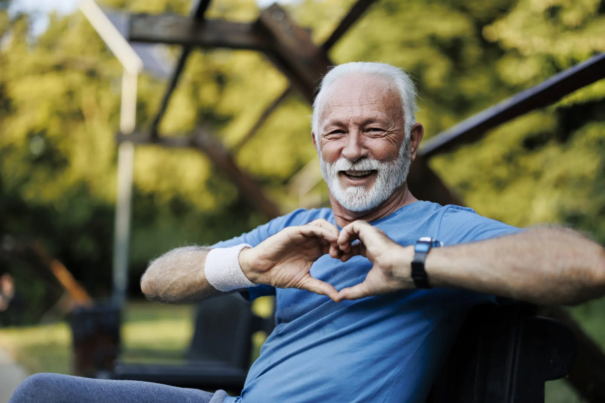A senior sporty man in nature showing a heart-shaped symbol