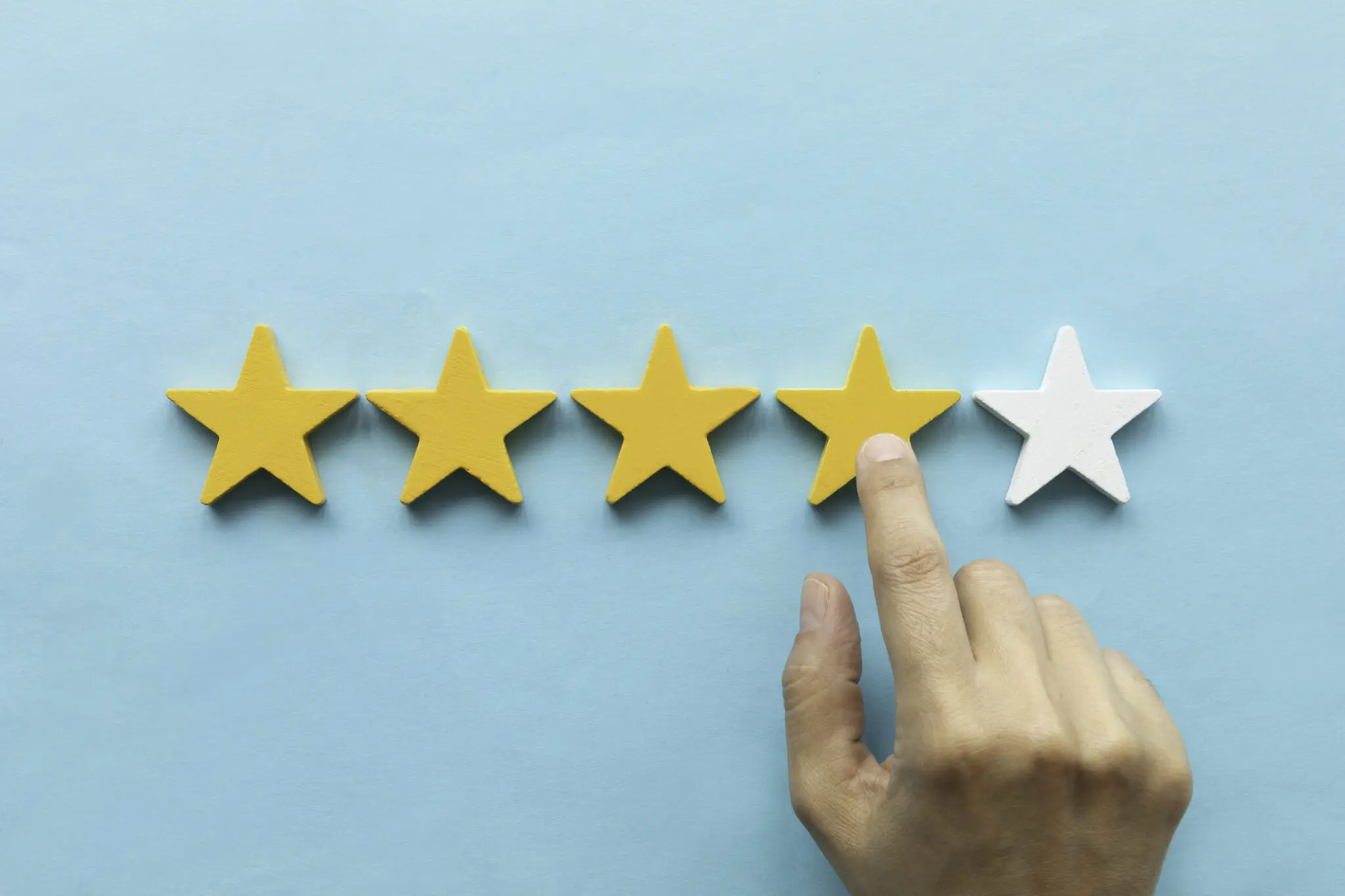 Hand is pointing at fourth star shape in front of blue background.