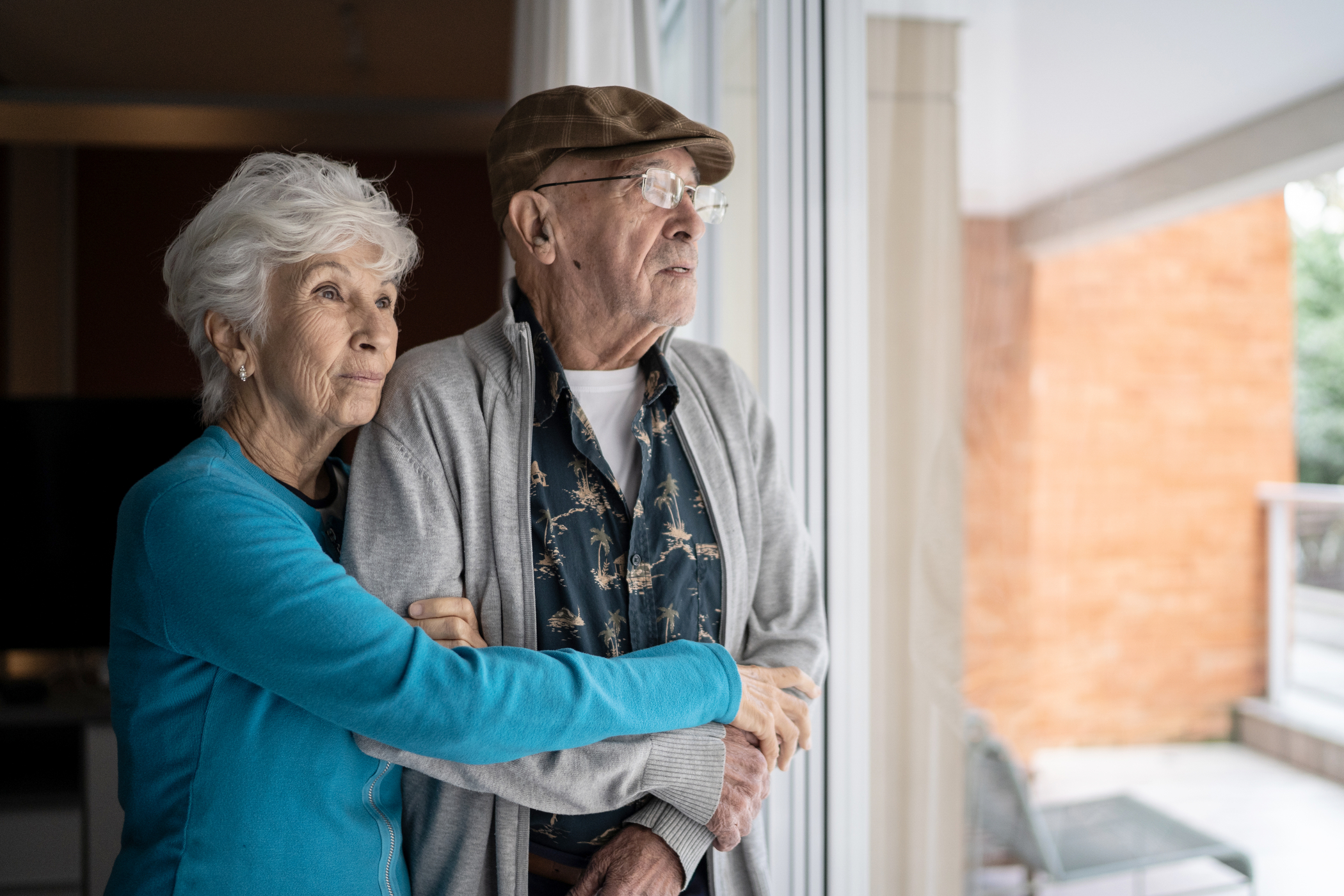 Senior couple hugging and standing by a sunny window
