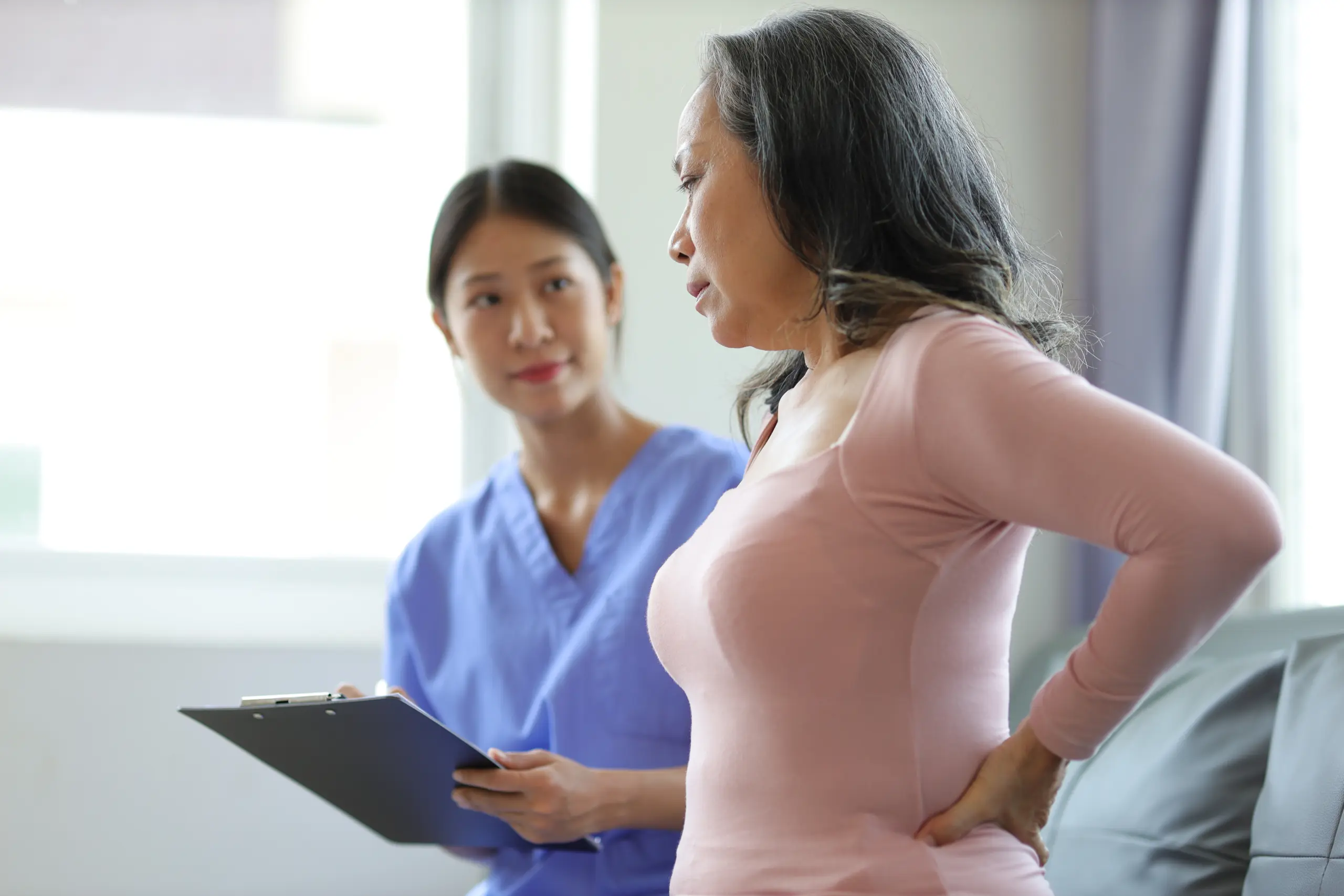 Young nurse taking notes for a middle-aged woman clutching at her back